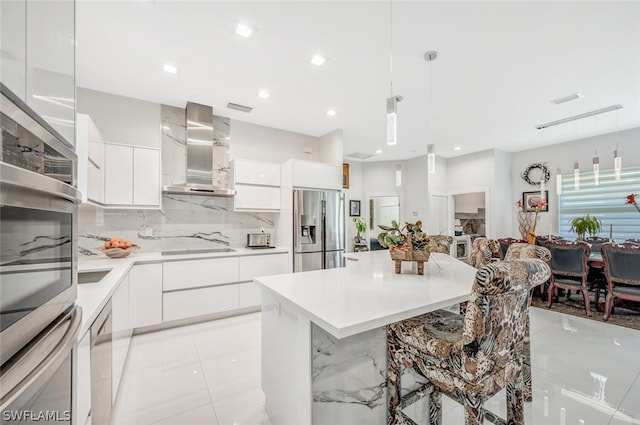 kitchen featuring stainless steel appliances, white cabinetry, wall chimney exhaust hood, and decorative light fixtures