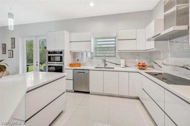 kitchen with stainless steel appliances, hanging light fixtures, white cabinetry, wall chimney exhaust hood, and sink