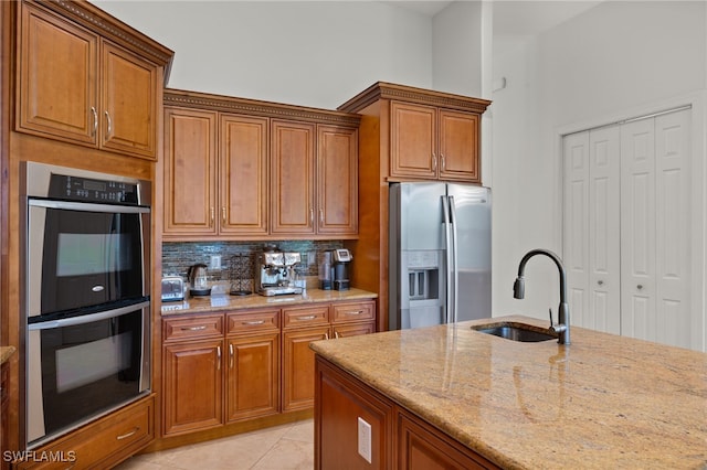 kitchen with light tile patterned floors, appliances with stainless steel finishes, backsplash, light stone counters, and sink