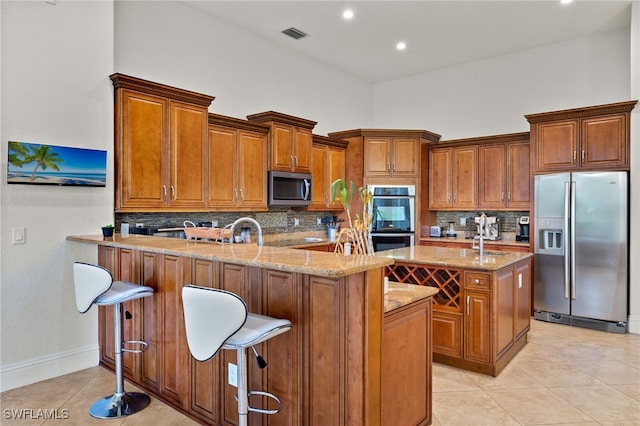 kitchen featuring appliances with stainless steel finishes, a towering ceiling, a kitchen bar, kitchen peninsula, and light tile patterned flooring