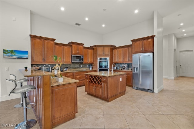 kitchen with kitchen peninsula, a high ceiling, light stone countertops, appliances with stainless steel finishes, and a breakfast bar area