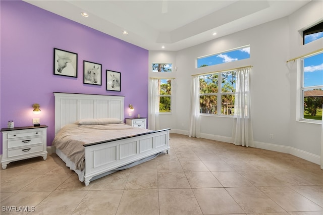 tiled bedroom with ceiling fan, a high ceiling, and a raised ceiling