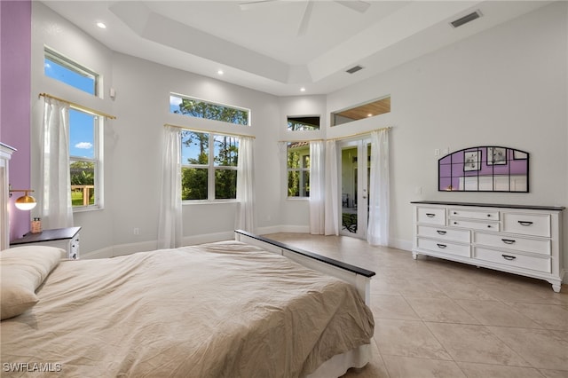 tiled bedroom with ceiling fan, a high ceiling, and a tray ceiling