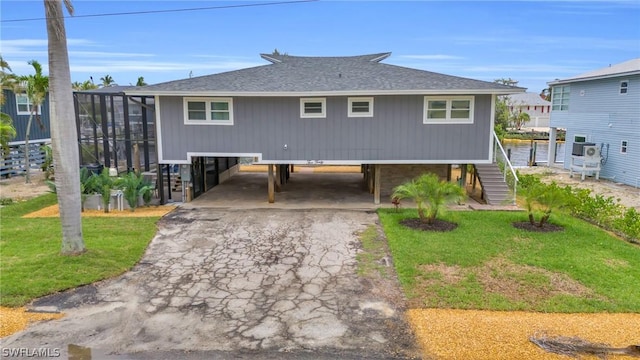 view of front facade with aphalt driveway, a shingled roof, glass enclosure, a carport, and a front lawn