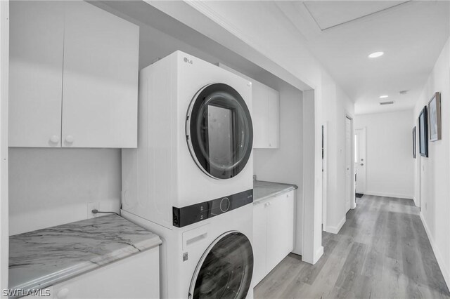 laundry room featuring cabinets, stacked washer and dryer, and light hardwood / wood-style flooring