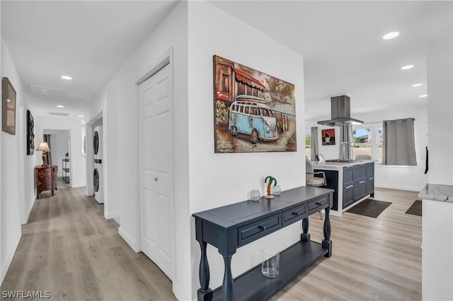 corridor featuring light wood-type flooring, recessed lighting, baseboards, and stacked washer and clothes dryer