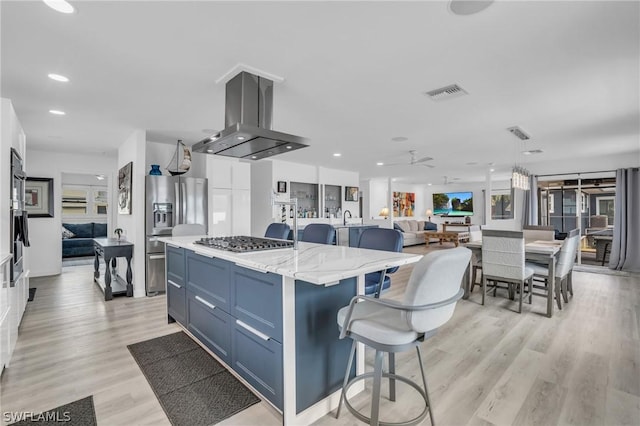 kitchen with light stone countertops, appliances with stainless steel finishes, island range hood, light hardwood / wood-style flooring, and a center island