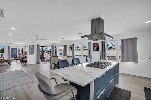 kitchen featuring ceiling fan, stainless steel gas cooktop, island exhaust hood, a kitchen island, and light wood-type flooring