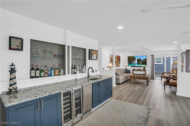 bar featuring blue cabinetry, light stone countertops, sink, and light hardwood / wood-style floors