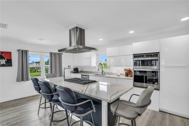 kitchen with appliances with stainless steel finishes, wall chimney exhaust hood, a kitchen island, sink, and white cabinetry