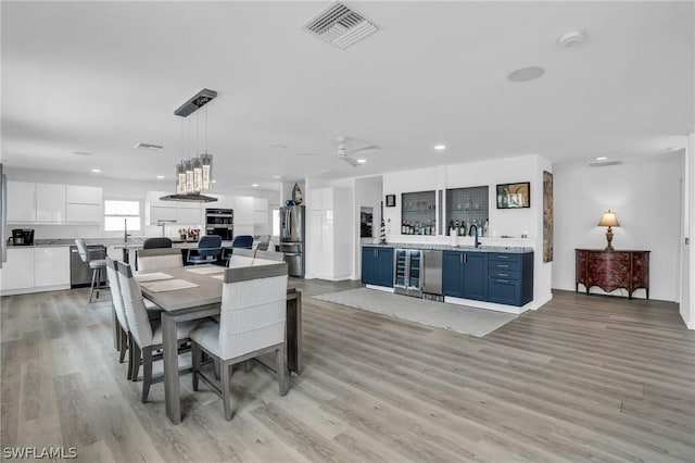 dining space with ceiling fan, light wood-type flooring, sink, and beverage cooler