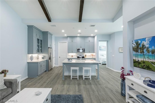 kitchen with hardwood / wood-style floors, backsplash, a kitchen breakfast bar, beam ceiling, and stainless steel appliances