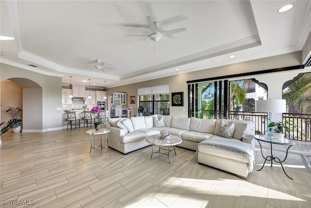 living room featuring a raised ceiling, ceiling fan, and crown molding