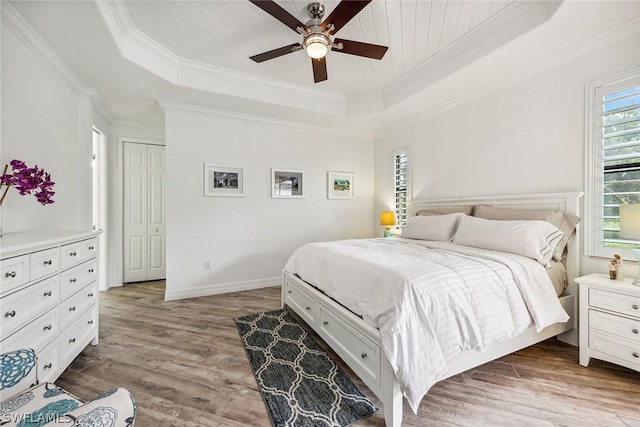 bedroom featuring ceiling fan, ornamental molding, light hardwood / wood-style flooring, a closet, and a tray ceiling