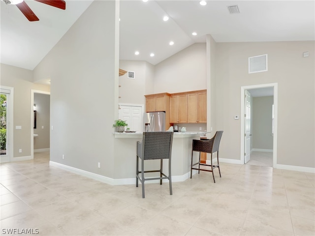 kitchen with high vaulted ceiling, kitchen peninsula, ceiling fan, a kitchen bar, and stainless steel fridge with ice dispenser