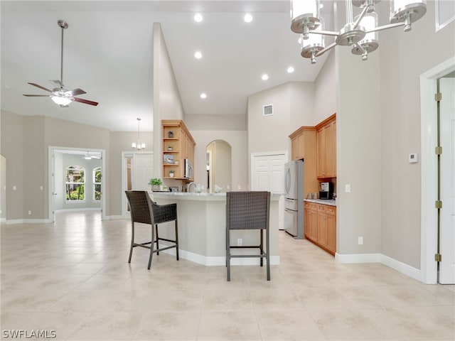 kitchen with stainless steel fridge, a towering ceiling, a kitchen breakfast bar, ceiling fan with notable chandelier, and light tile patterned floors