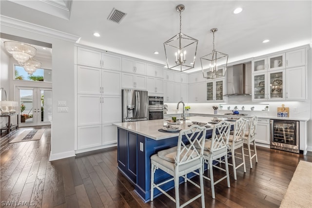 kitchen featuring stainless steel appliances, beverage cooler, white cabinets, a kitchen island with sink, and wall chimney range hood