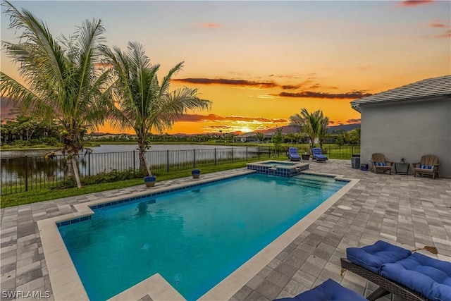 pool at dusk with a water view, a fenced backyard, a pool with connected hot tub, and a patio