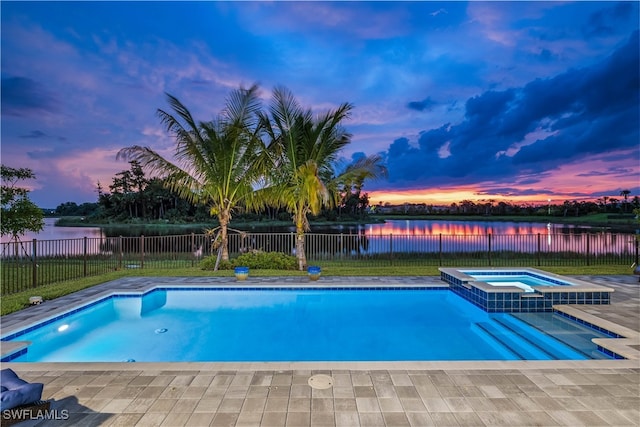 pool at dusk featuring an in ground hot tub and a water view