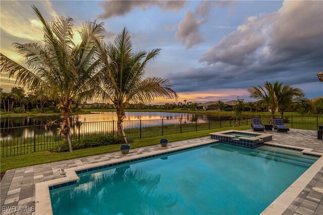 pool at dusk featuring a water view, a yard, and an in ground hot tub