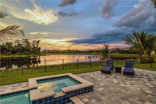 pool at dusk with a patio area, a water view, a lawn, and an in ground hot tub