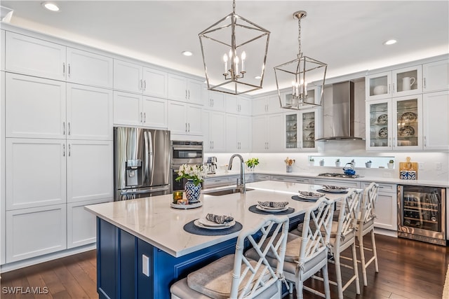 kitchen featuring beverage cooler, wall chimney exhaust hood, sink, an island with sink, and appliances with stainless steel finishes