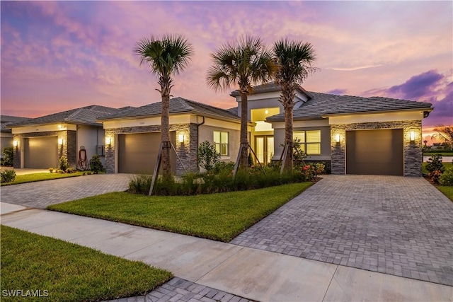 prairie-style house with an attached garage, stone siding, a lawn, and decorative driveway