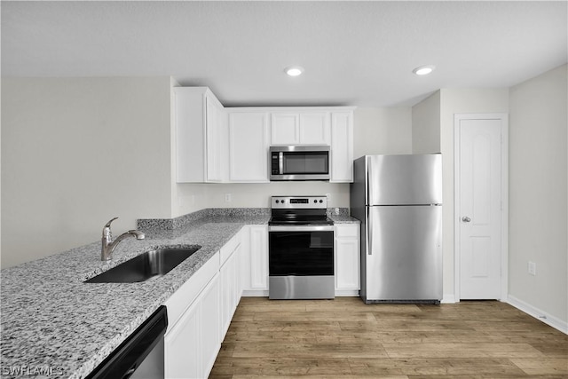 kitchen with light stone countertops, white cabinetry, sink, stainless steel appliances, and light hardwood / wood-style flooring