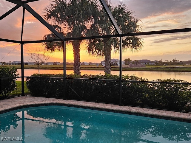 pool at dusk featuring a water view and glass enclosure