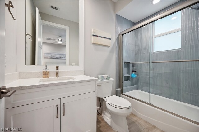 full bathroom featuring bath / shower combo with glass door, vanity, toilet, and ceiling fan