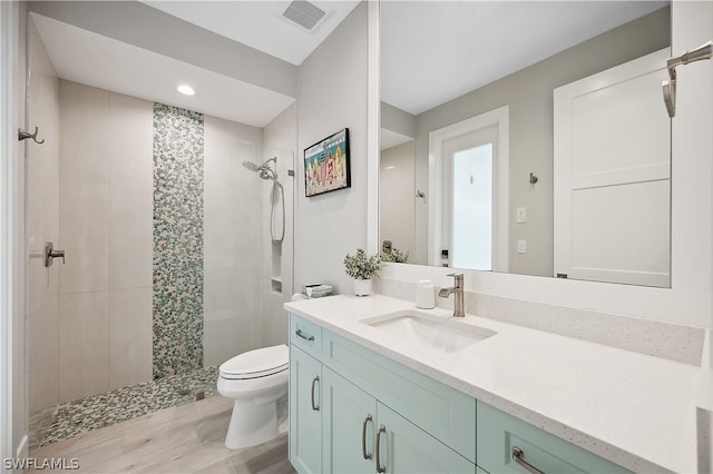 bathroom with a tile shower, toilet, and vanity