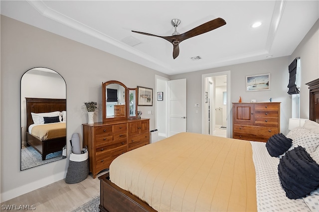 bedroom with a raised ceiling, ceiling fan, ensuite bath, and wood-type flooring