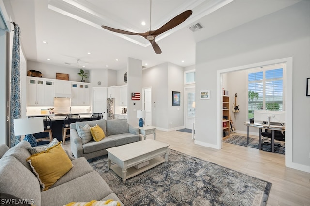 living room with light wood-type flooring, a high ceiling, and ceiling fan