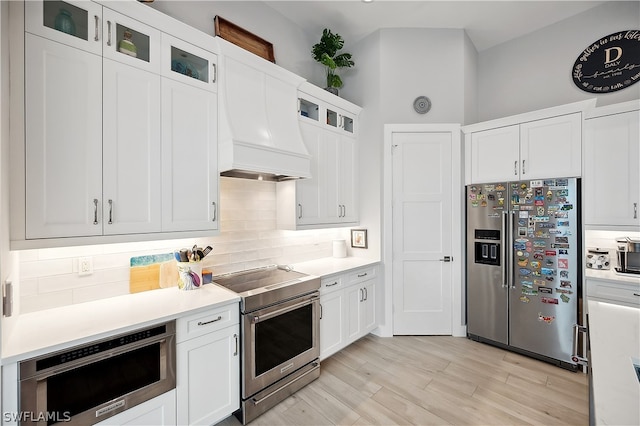 kitchen with premium appliances, custom exhaust hood, backsplash, and white cabinetry