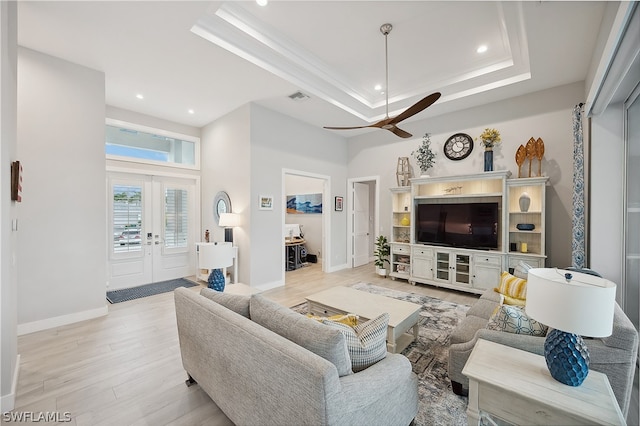 living room featuring light wood-type flooring, a tray ceiling, french doors, and ceiling fan