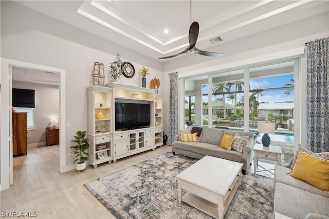 living room with ceiling fan, a tray ceiling, and light wood-type flooring