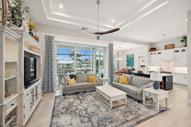 living room featuring a raised ceiling, ceiling fan with notable chandelier, and light hardwood / wood-style floors