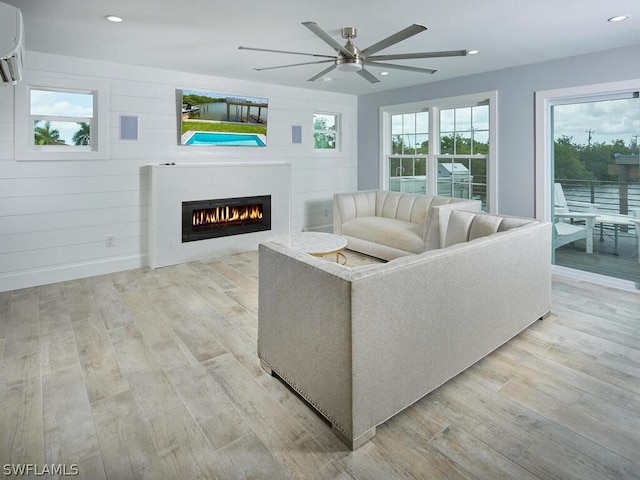 living room with light hardwood / wood-style flooring, an AC wall unit, and ceiling fan