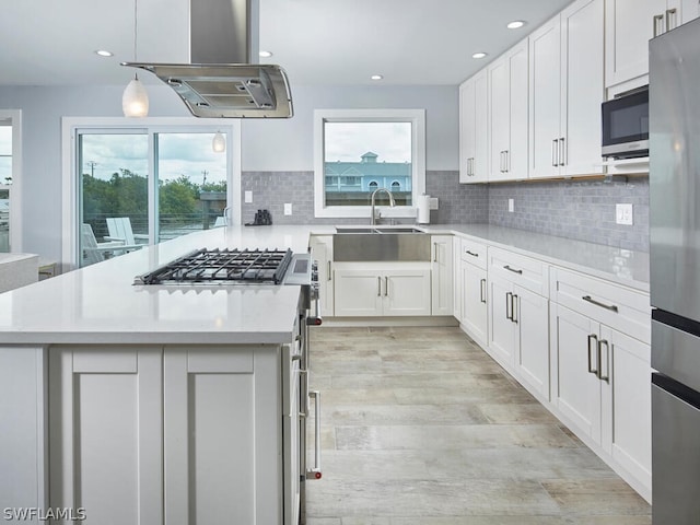 kitchen featuring stainless steel refrigerator, hanging light fixtures, island range hood, a healthy amount of sunlight, and white cabinets