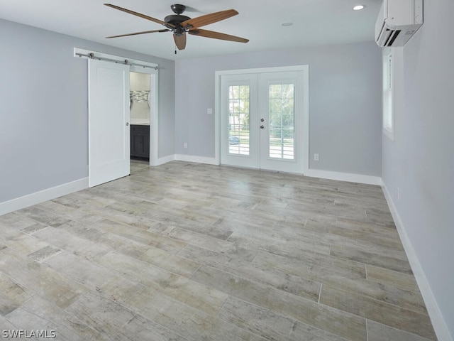 empty room featuring a wall mounted air conditioner, light wood-type flooring, a barn door, and french doors