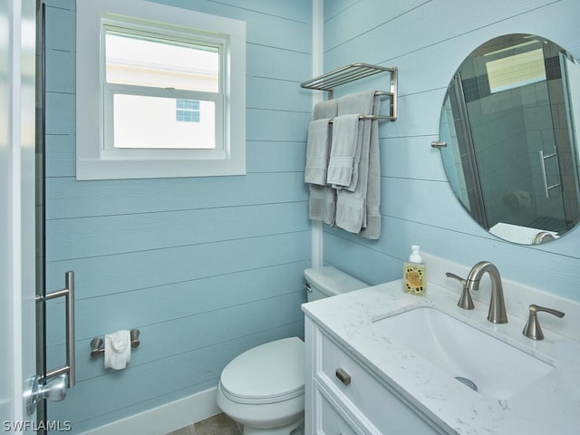 bathroom featuring toilet, vanity, wooden walls, and a shower with door