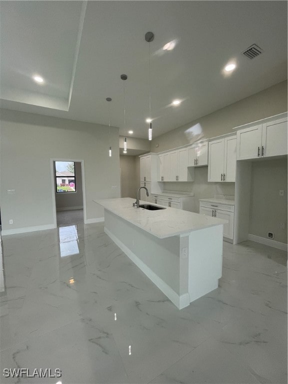 kitchen featuring white cabinetry, light stone countertops, pendant lighting, sink, and a spacious island