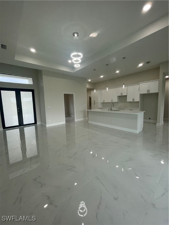 unfurnished living room featuring a raised ceiling, sink, a chandelier, and french doors