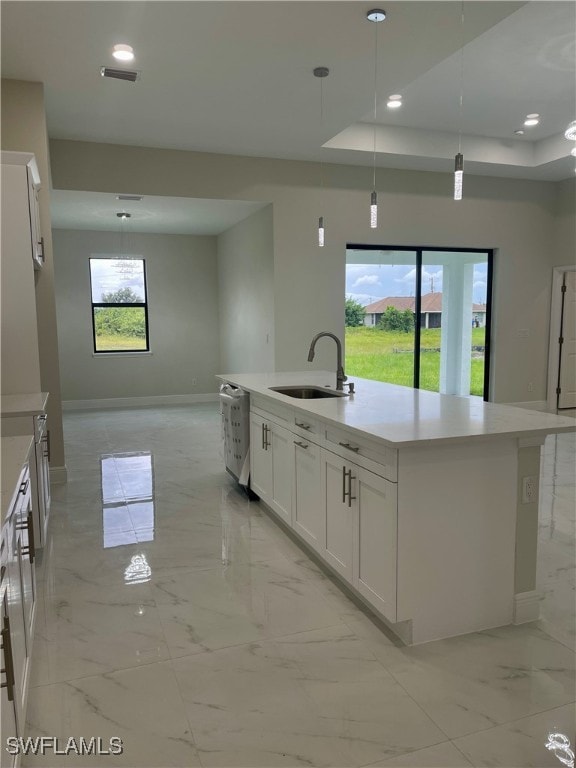 kitchen featuring hanging light fixtures, white cabinets, a tray ceiling, a center island with sink, and sink