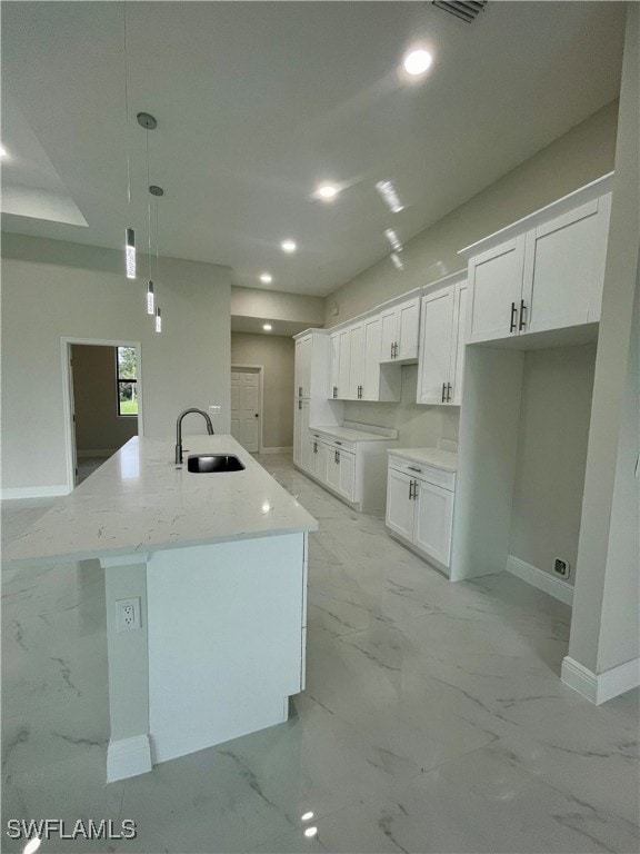 kitchen with light stone counters, white cabinets, pendant lighting, sink, and a center island with sink