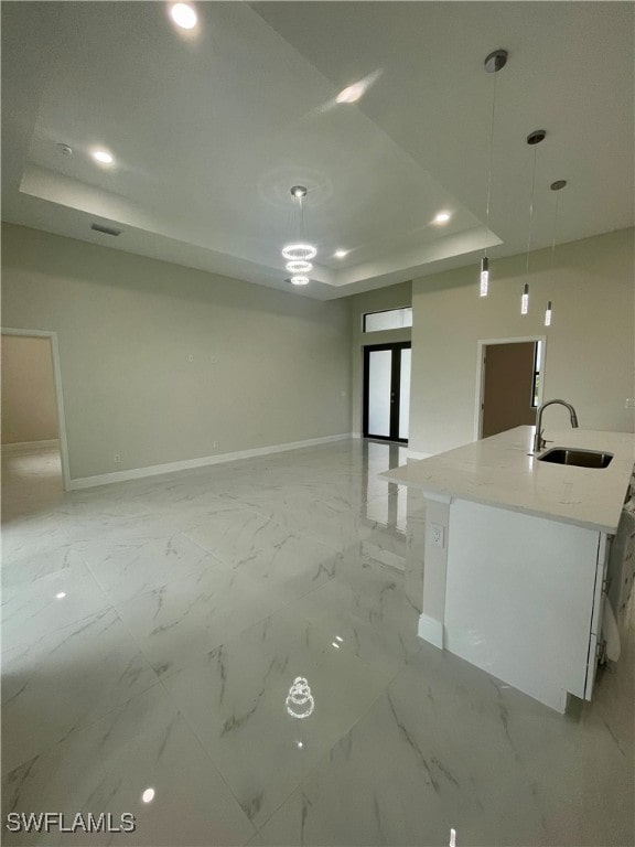 kitchen featuring a center island with sink, a tray ceiling, sink, and decorative light fixtures