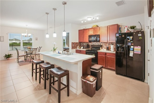 kitchen with pendant lighting, a center island with sink, light tile patterned floors, and black appliances