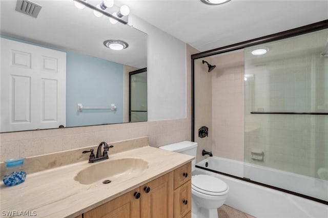 full bathroom with tasteful backsplash, combined bath / shower with glass door, toilet, vanity, and tile walls