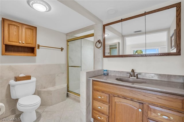 bathroom with vanity, tile patterned floors, toilet, tile walls, and a shower with shower door