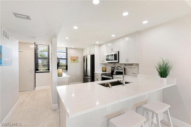 kitchen featuring white cabinetry, kitchen peninsula, a breakfast bar area, stainless steel appliances, and sink